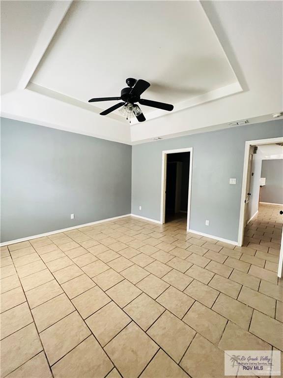 spare room featuring a tray ceiling, a ceiling fan, baseboards, and visible vents