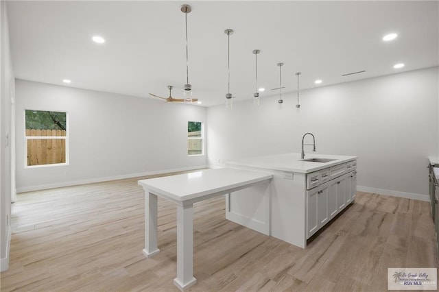 kitchen with a kitchen island with sink, sink, pendant lighting, and light wood-type flooring