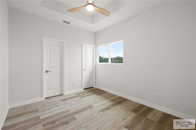 unfurnished bedroom featuring ceiling fan, light hardwood / wood-style floors, and a tray ceiling