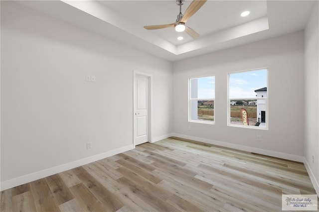 spare room featuring a tray ceiling, ceiling fan, and light hardwood / wood-style floors