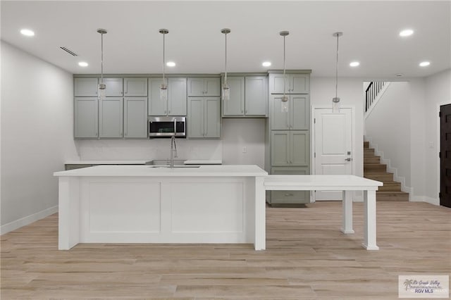 kitchen with pendant lighting, light hardwood / wood-style floors, a center island with sink, and sink