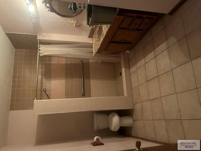 bathroom with a textured wall and a tile shower