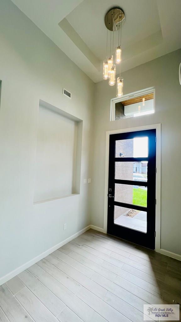 foyer with a chandelier, light wood-type flooring, and a tray ceiling