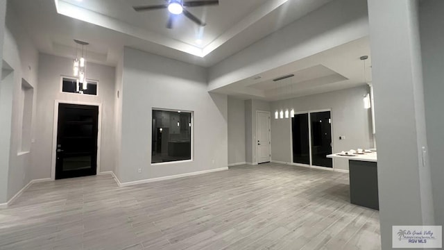 interior space featuring ceiling fan, light hardwood / wood-style flooring, a high ceiling, and a tray ceiling