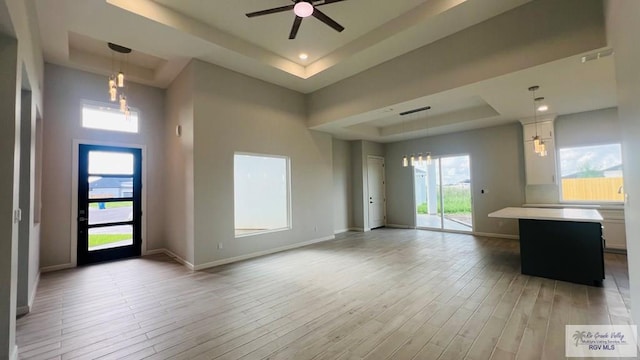 unfurnished living room with a tray ceiling, a wealth of natural light, light hardwood / wood-style floors, and ceiling fan with notable chandelier