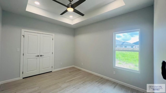 unfurnished bedroom featuring a closet, light hardwood / wood-style floors, a raised ceiling, and ceiling fan