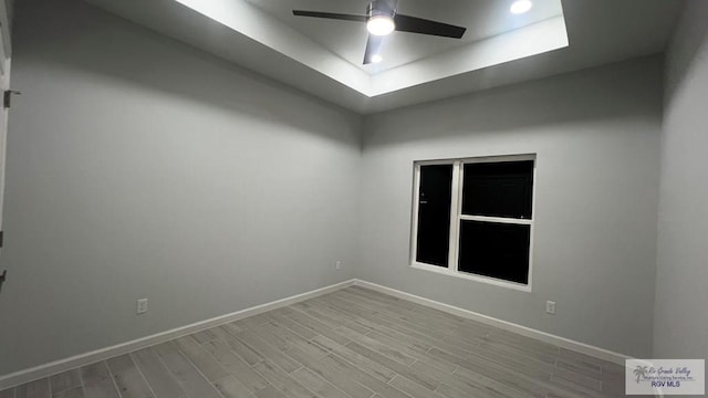 spare room with a raised ceiling, ceiling fan, and light hardwood / wood-style floors