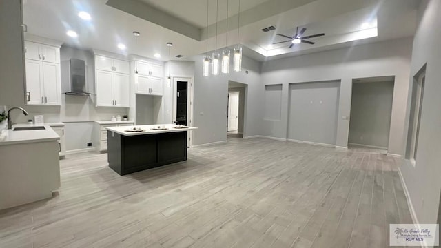 kitchen featuring a tray ceiling, a kitchen island, wall chimney range hood, and light wood-type flooring