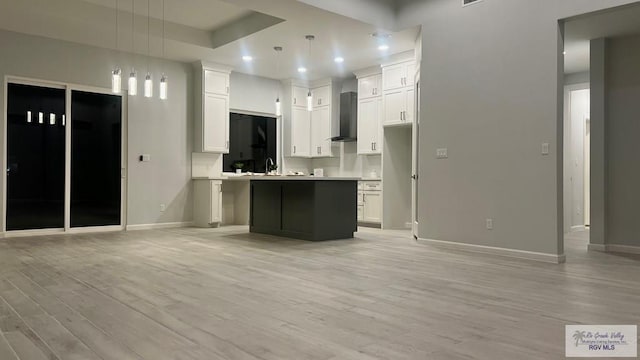 kitchen with white cabinets, hanging light fixtures, wall chimney range hood, and an island with sink