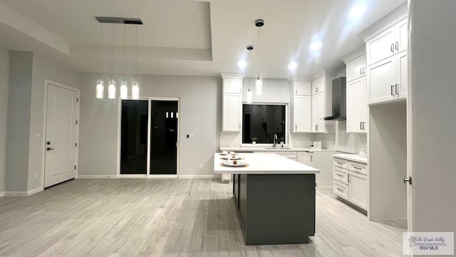 kitchen featuring white cabinets, pendant lighting, a center island, and wall chimney exhaust hood