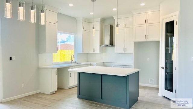 kitchen with wall chimney exhaust hood, sink, white cabinets, a center island, and hanging light fixtures