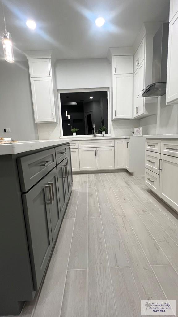 kitchen with white cabinetry, sink, light hardwood / wood-style floors, and wall chimney range hood