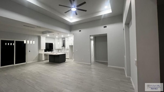 unfurnished living room with ceiling fan, light wood-type flooring, a towering ceiling, and a tray ceiling