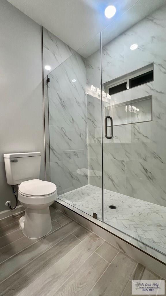 bathroom featuring a shower with door and toilet