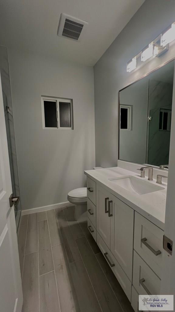 bathroom featuring vanity, hardwood / wood-style flooring, toilet, and a shower with shower door