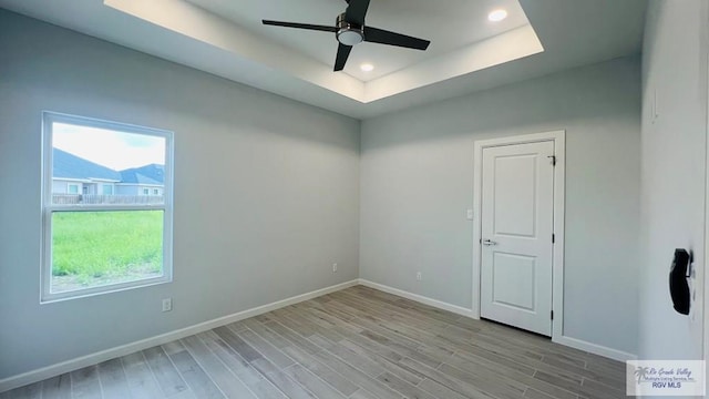 empty room featuring ceiling fan, a raised ceiling, and light hardwood / wood-style flooring