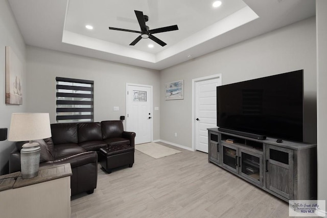 living room featuring a tray ceiling, light wood finished floors, recessed lighting, ceiling fan, and baseboards