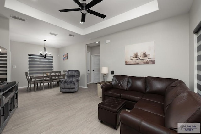 living room with baseboards, visible vents, a tray ceiling, light wood-type flooring, and ceiling fan with notable chandelier