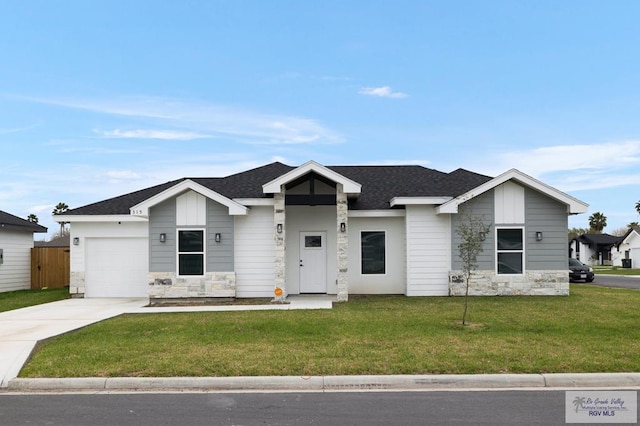 view of front facade featuring roof with shingles, a front yard, a garage, stone siding, and driveway