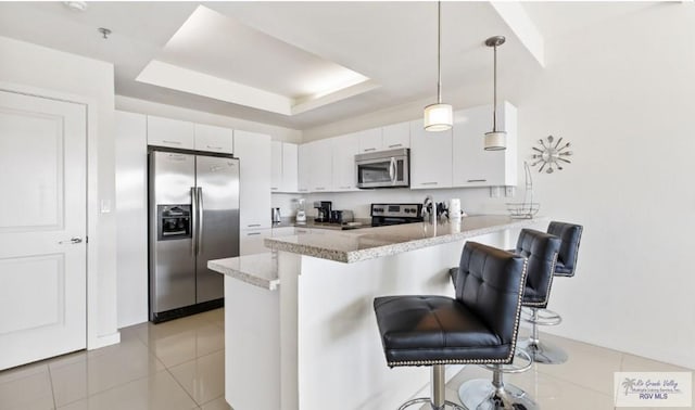 kitchen with a kitchen bar, appliances with stainless steel finishes, kitchen peninsula, white cabinetry, and hanging light fixtures