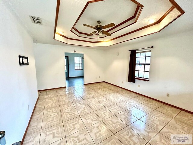 tiled spare room featuring a tray ceiling, ceiling fan, and crown molding