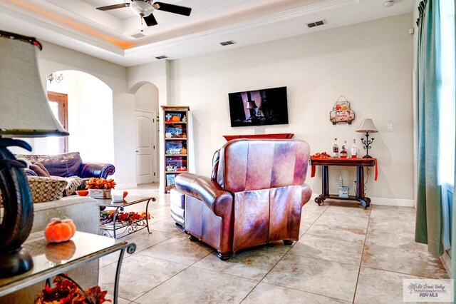 tiled living room with ceiling fan, a healthy amount of sunlight, a raised ceiling, and ornamental molding