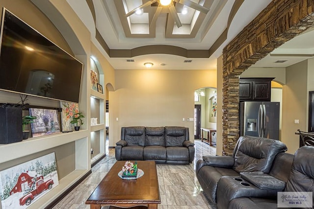 living area with arched walkways, ceiling fan, a tray ceiling, and visible vents