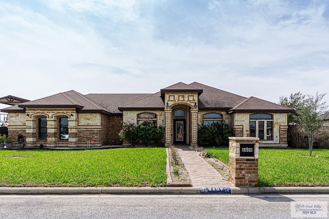 french country inspired facade with a front yard, stone siding, and brick siding