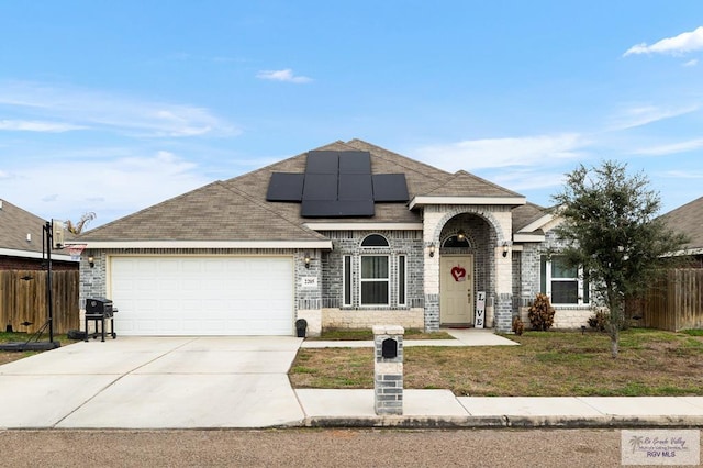 french country home with brick siding, solar panels, an attached garage, fence, and driveway