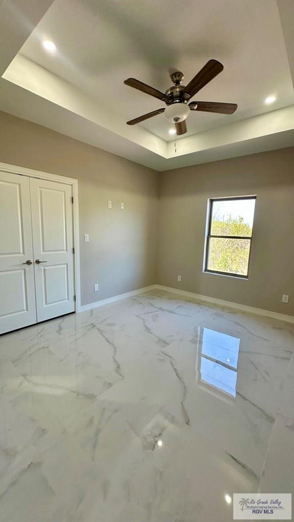 unfurnished room featuring recessed lighting, baseboards, a raised ceiling, and marble finish floor