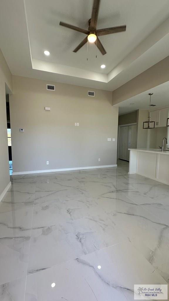 unfurnished living room with visible vents, marble finish floor, baseboards, and a tray ceiling