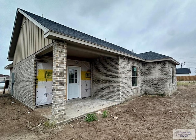 exterior space featuring a patio, brick siding, board and batten siding, and a shingled roof