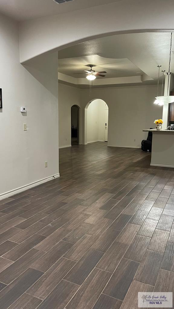 unfurnished living room featuring a raised ceiling, ceiling fan, and dark hardwood / wood-style floors