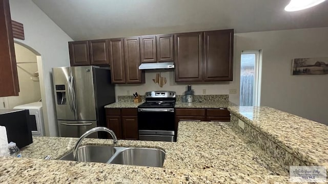 kitchen with appliances with stainless steel finishes, light stone counters, vaulted ceiling, sink, and washer / dryer