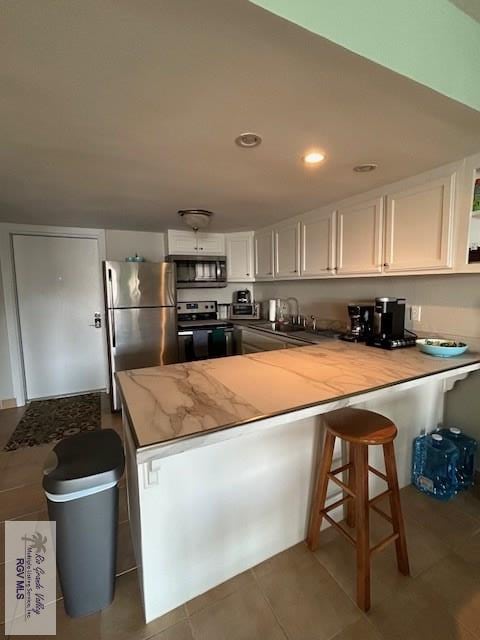 kitchen featuring dark tile patterned flooring, white cabinets, a kitchen bar, kitchen peninsula, and stainless steel appliances