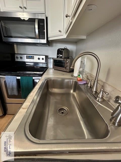 interior details featuring white cabinetry, stainless steel appliances, and sink