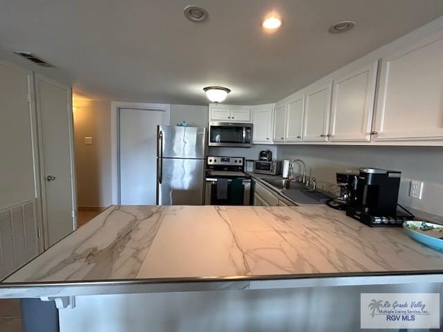 kitchen featuring sink, light stone counters, kitchen peninsula, stainless steel appliances, and white cabinets