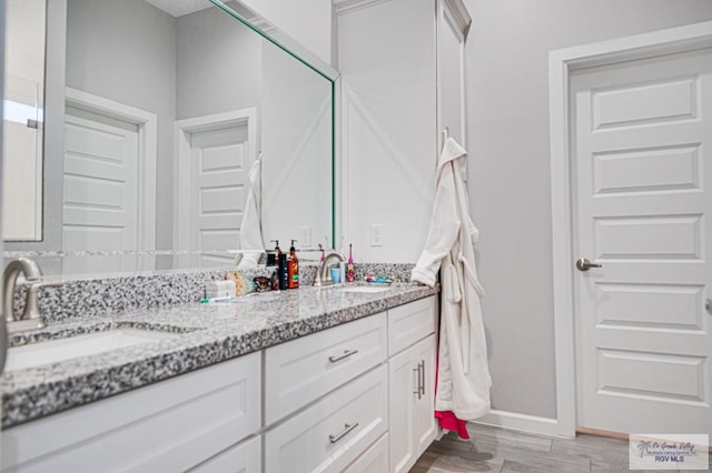 bathroom with double vanity, wood finished floors, a sink, and baseboards