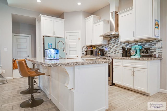 kitchen with white cabinets, a kitchen island with sink, and wall chimney range hood