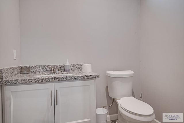 half bath with baseboards, vanity, and toilet