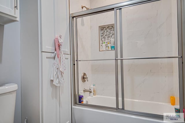 bathroom featuring toilet and shower / bath combination with glass door