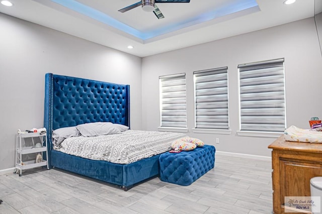 bedroom featuring light wood-type flooring, a raised ceiling, and baseboards