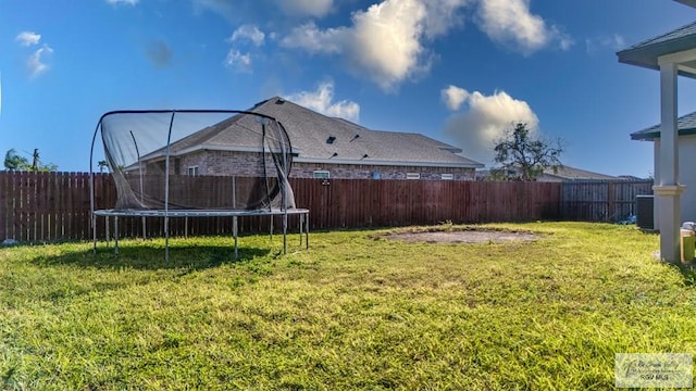 view of yard with a trampoline, a fenced backyard, and central AC