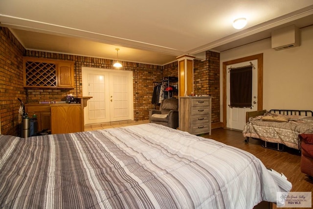 bedroom featuring ornate columns, brick wall, wood finished floors, and a wall mounted AC