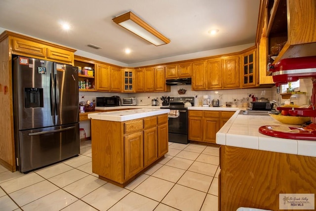 kitchen featuring tile counters, stainless steel fridge with ice dispenser, black electric range oven, under cabinet range hood, and a sink