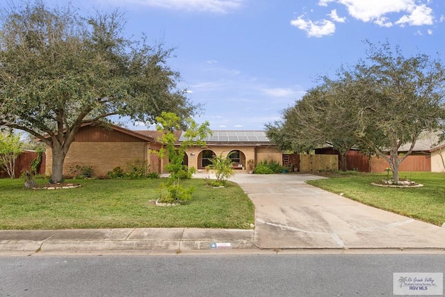view of front facade with brick siding, fence, a front yard, roof mounted solar panels, and driveway
