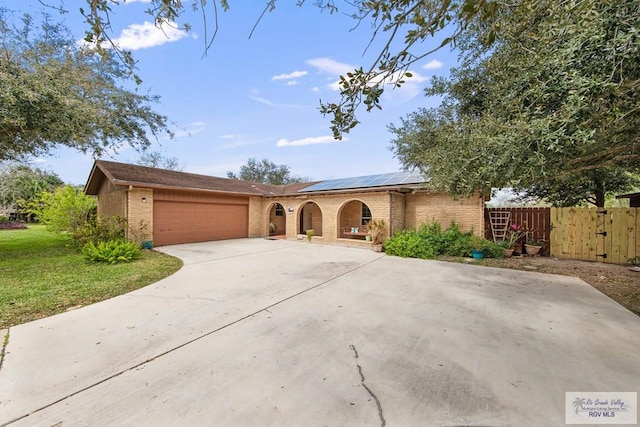 ranch-style home featuring brick siding, fence, roof mounted solar panels, driveway, and an attached garage