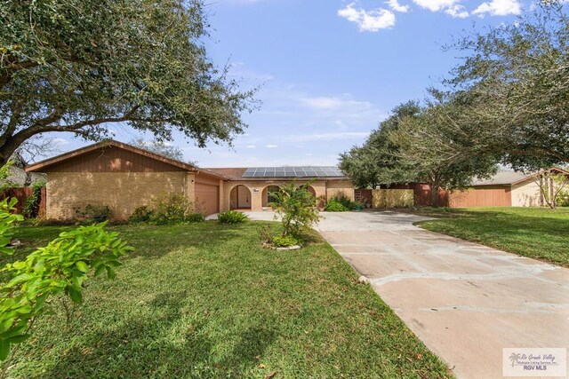 view of front of house featuring a garage, solar panels, brick siding, fence, and driveway