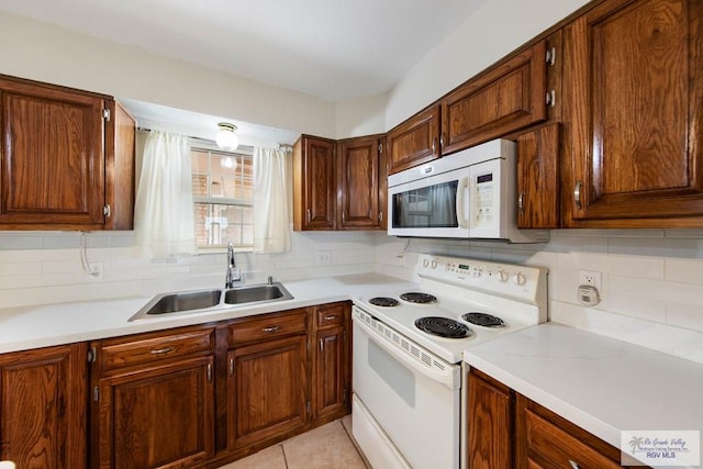 kitchen with white appliances, backsplash, light countertops, and a sink