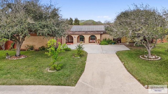 mediterranean / spanish-style home featuring brick siding, roof mounted solar panels, driveway, and a front yard